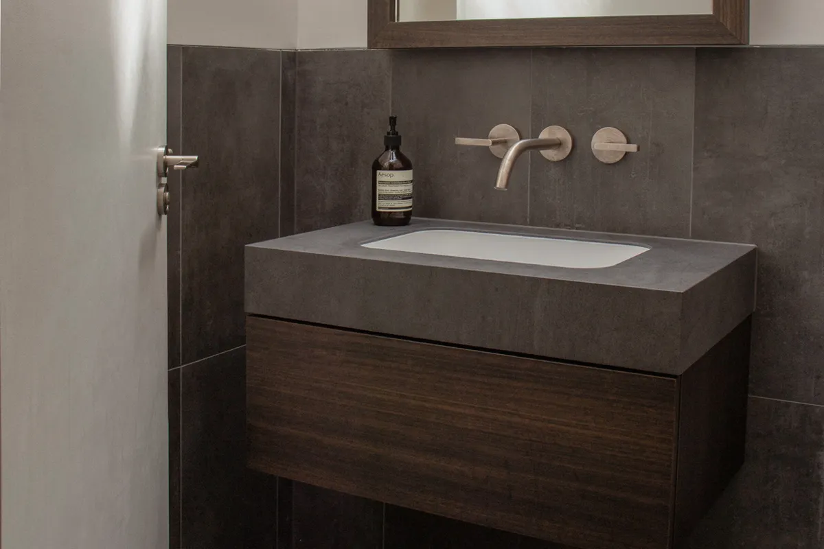 Bespoke wall-hung bathroom vanity unit in dark walnut with a concrete-effect stone worktop, undermount basin and brushed gold wall-mounted tap