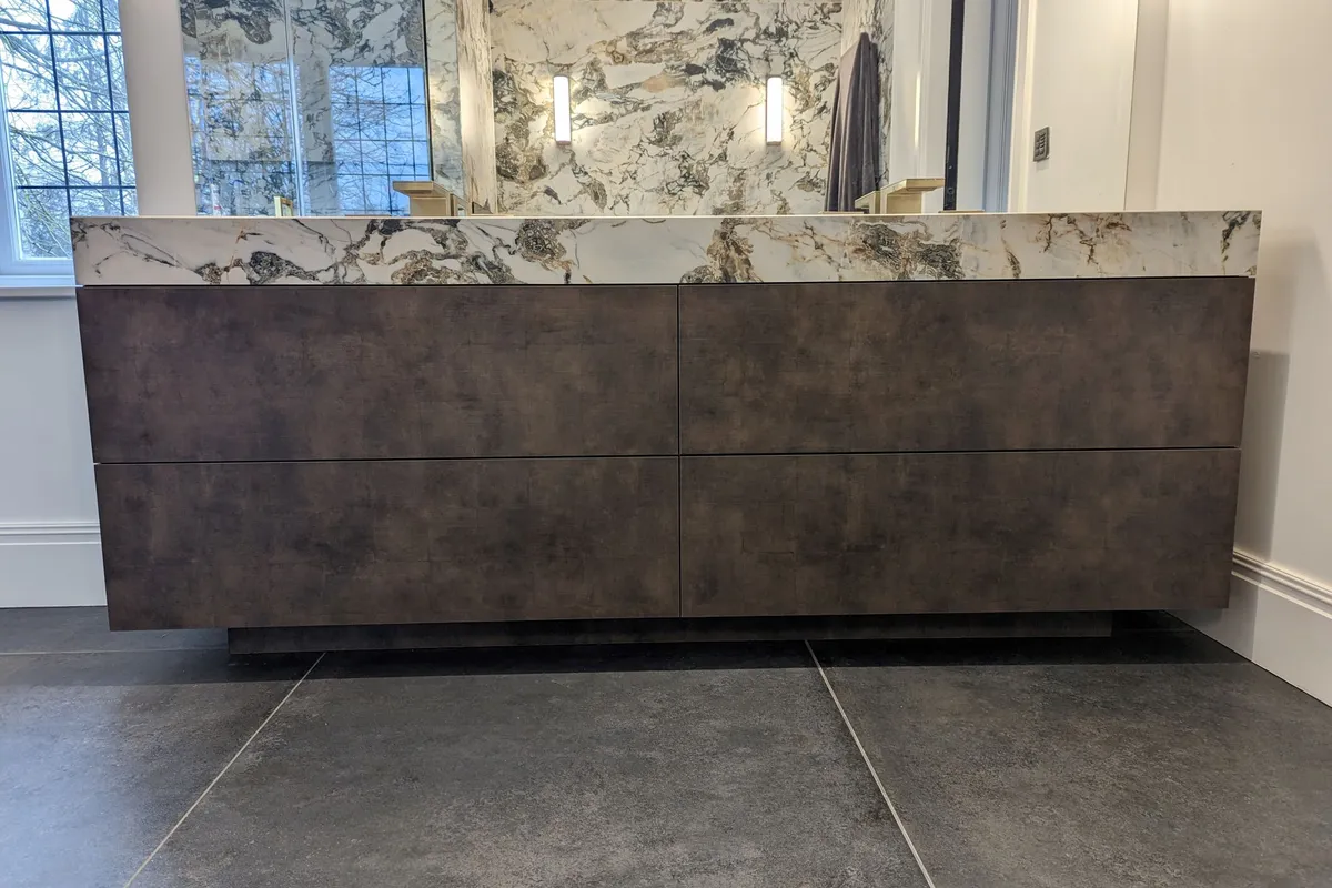 Bespoke bathroom vanity unit with brushed bronze finish, six handleless drawers and a book-matched marble worktop with integrated double basin
