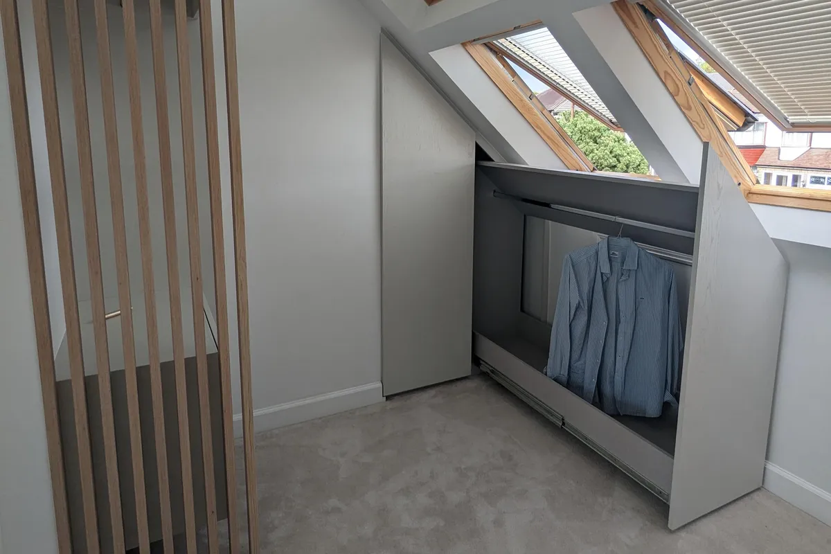 Bespoke loft wardrobe with hanging rail built into a sloped ceiling space, light grey finish with Velux windows above