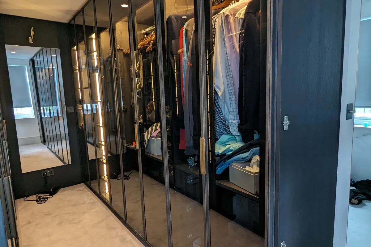 Bespoke walk-in wardrobe with smoked glass and bronze framed doors, integrated LED lighting and full-length hanging rails