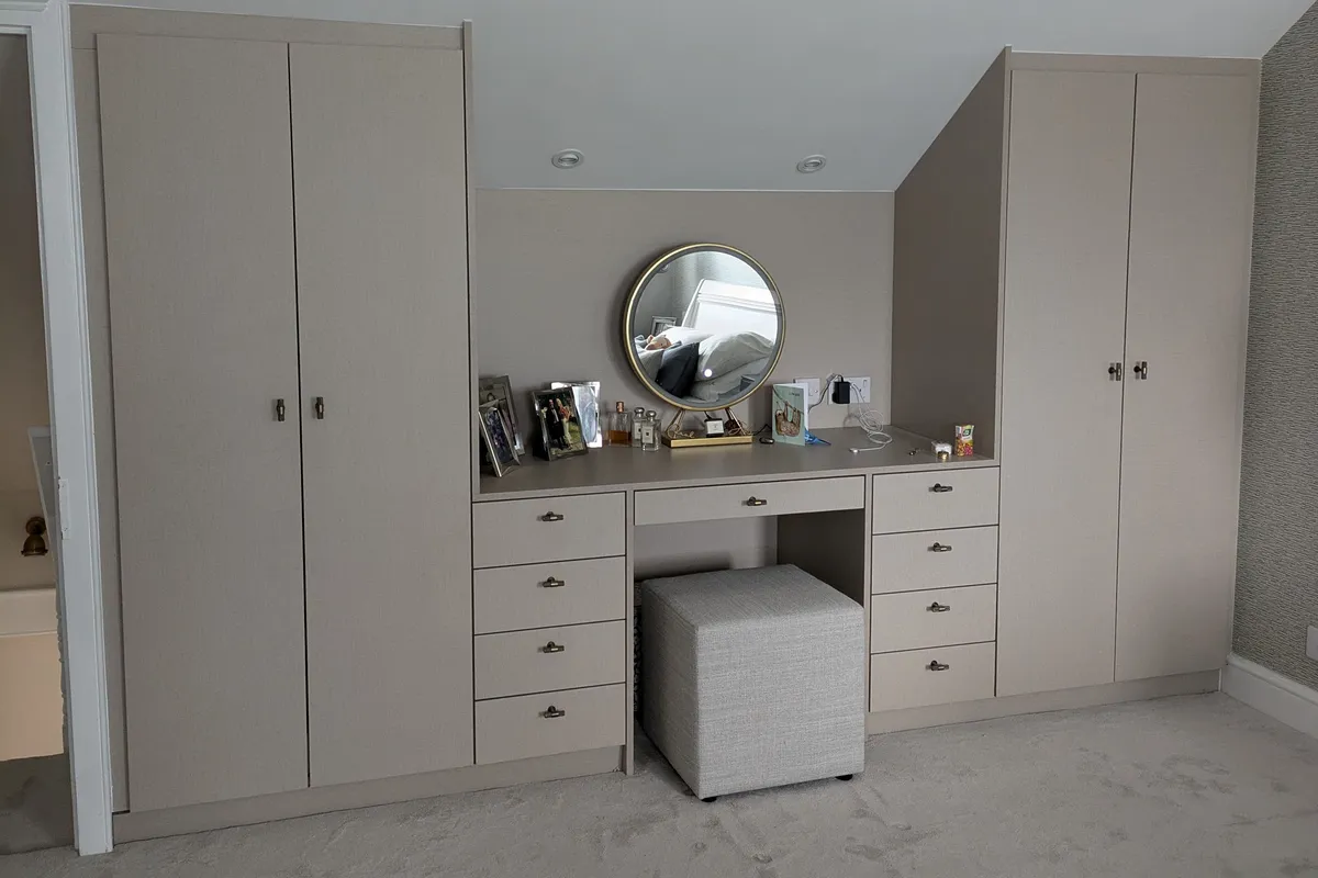 Bespoke fitted loft wardrobe with integrated dressing table, stone grey finish and cup-pull handles